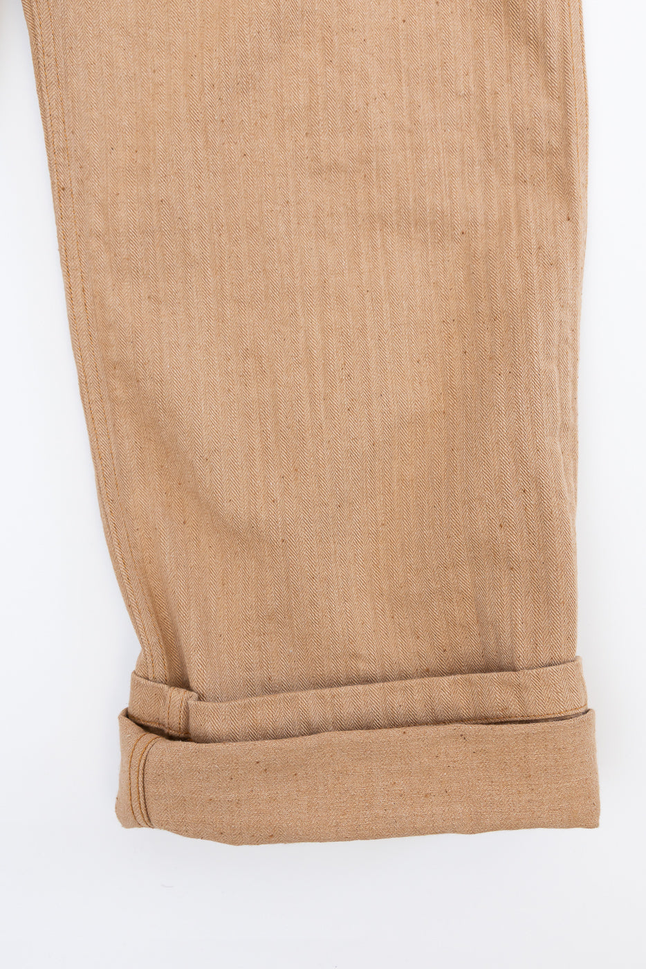 Close-up of tan herringbone selvedge pants leg, front view, showing cuffed hem detail and fabric texture