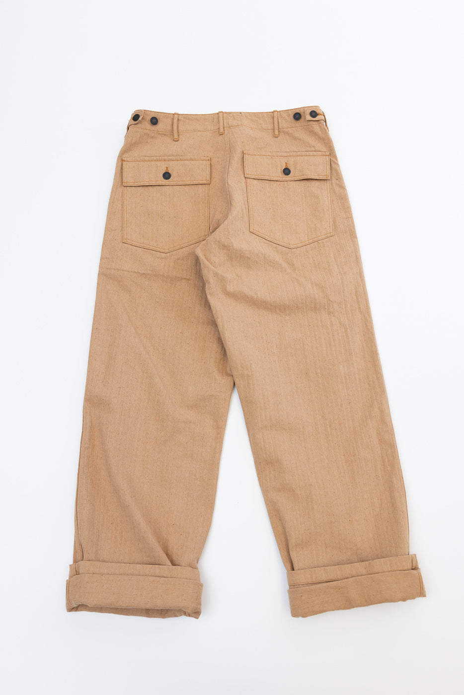 Back view flat lay of tan selvedge work pants with buttoned rear pockets, cuffed hems, and visible fabric texture