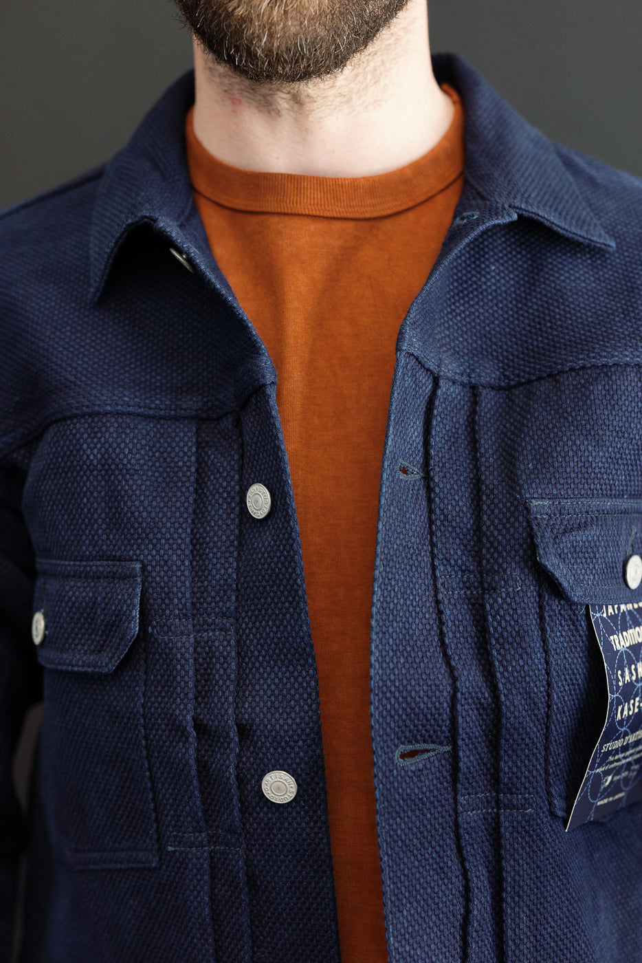 Close-up front view of navy textured jacket with buttons, worn by male model over orange tee