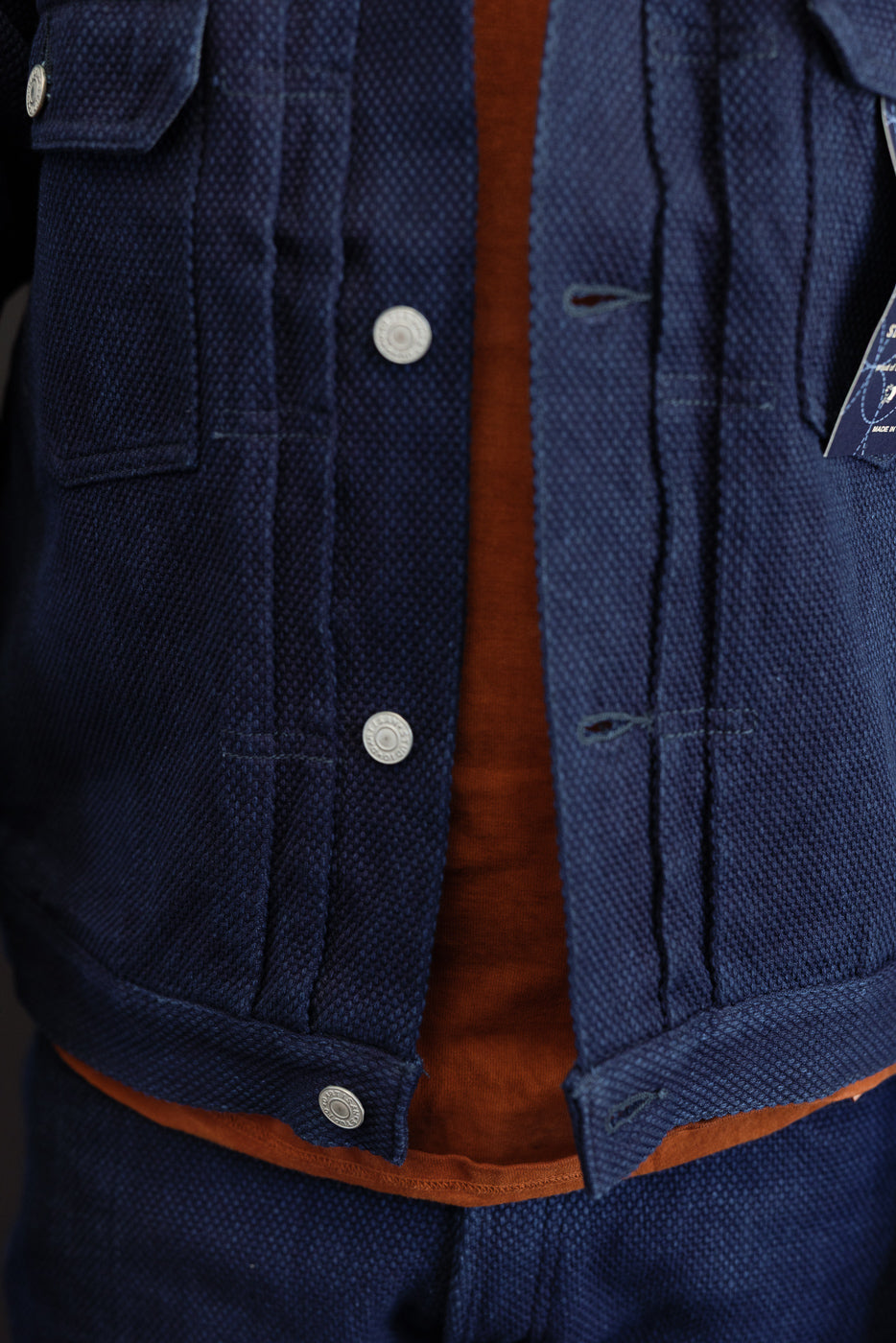 Close-up front view of navy jacket with silver buttons, textured fabric, and orange lining, worn by male model.