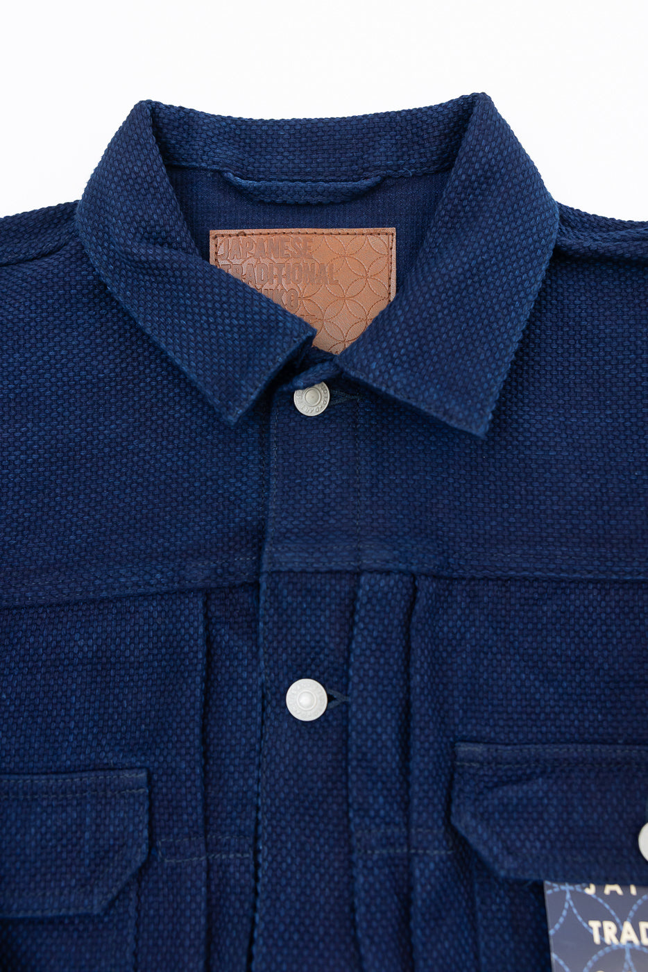 Close-up front view of navy shirt collar, buttons, and leather tag, showcasing fabric texture and design details.