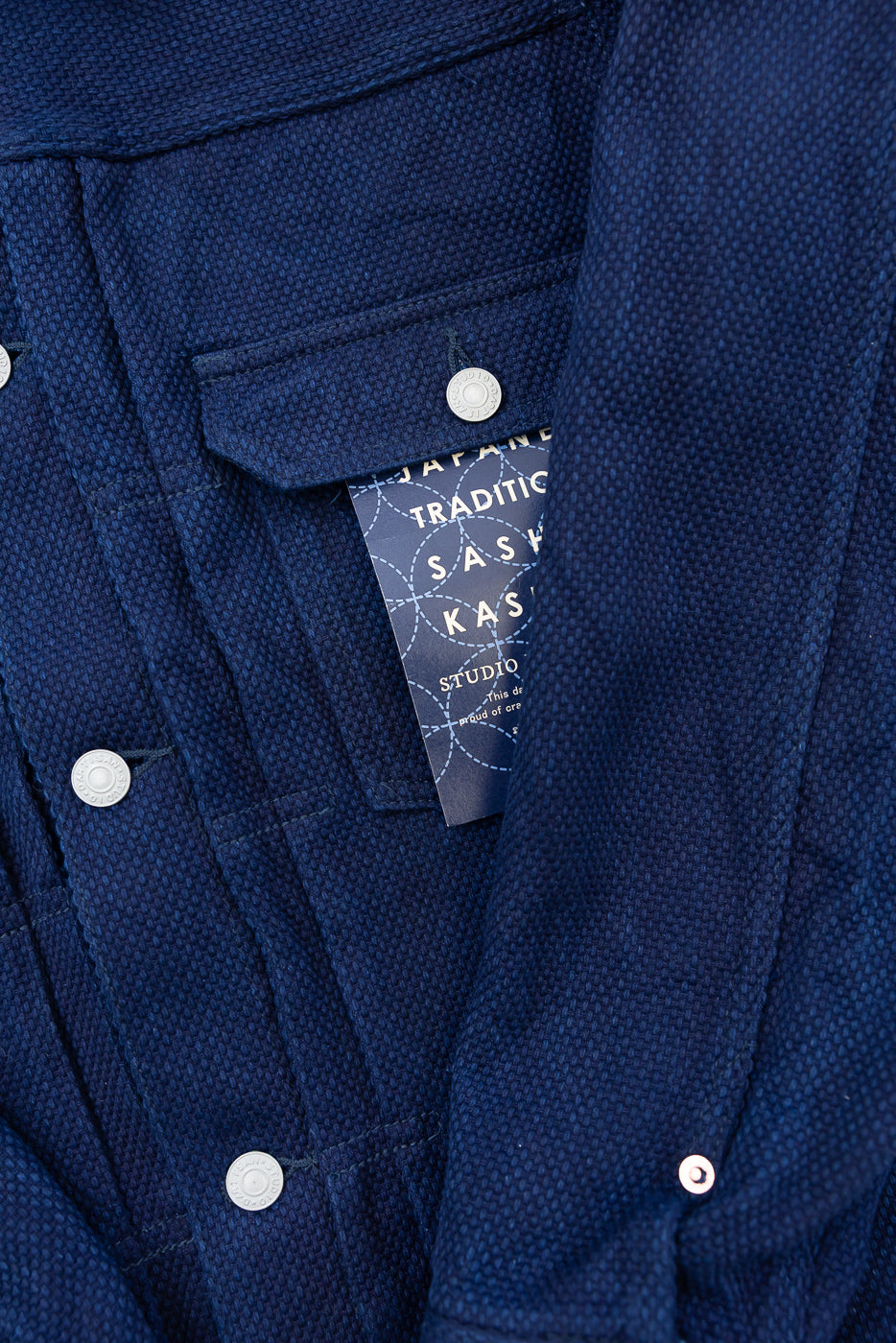 Close-up of navy jacket front, showing textured fabric, silver buttons, and brand tag detail.