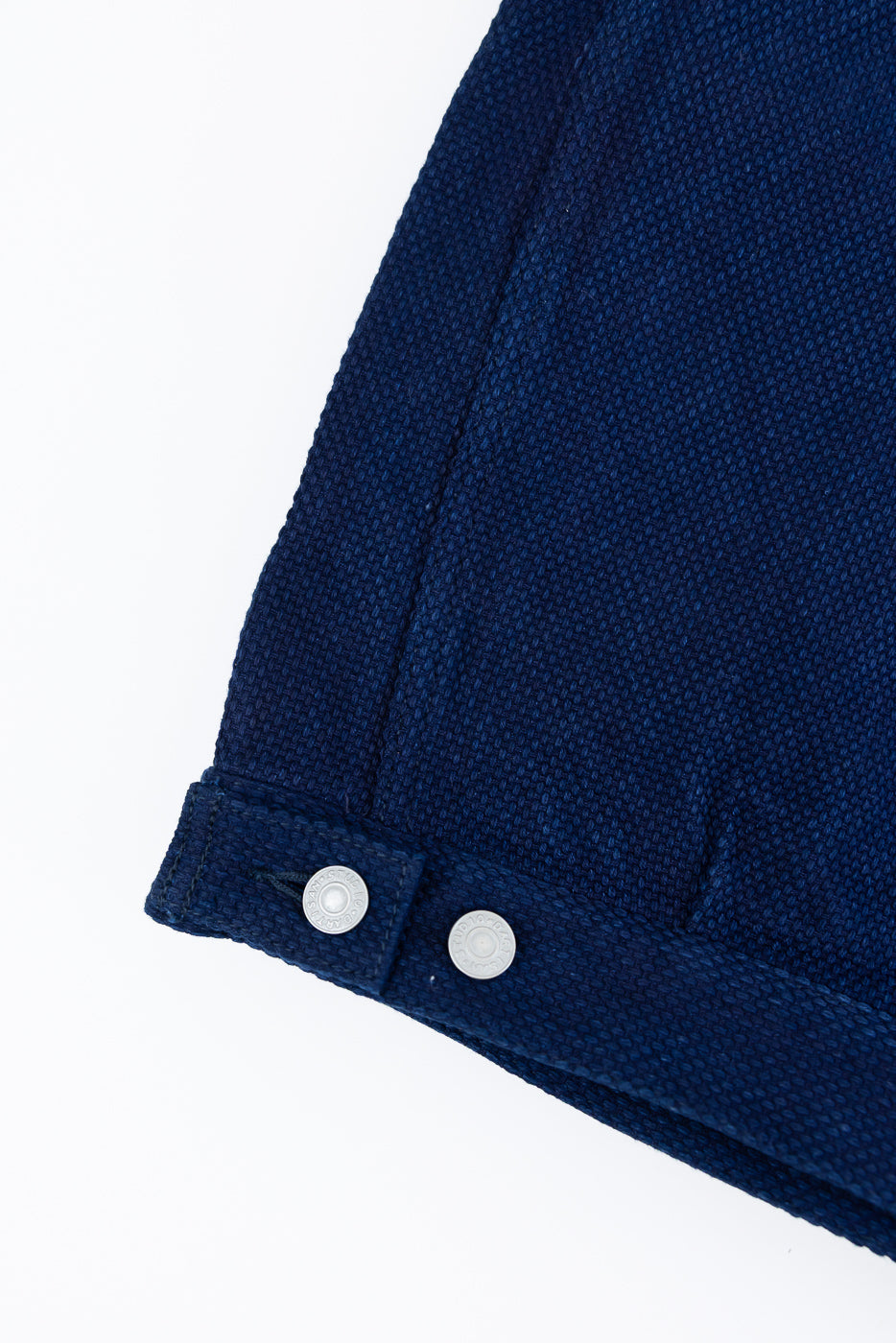 Close-up of navy blue shirt sleeve cuff with two silver buttons, showcasing textured fabric weave and clean hem detail.