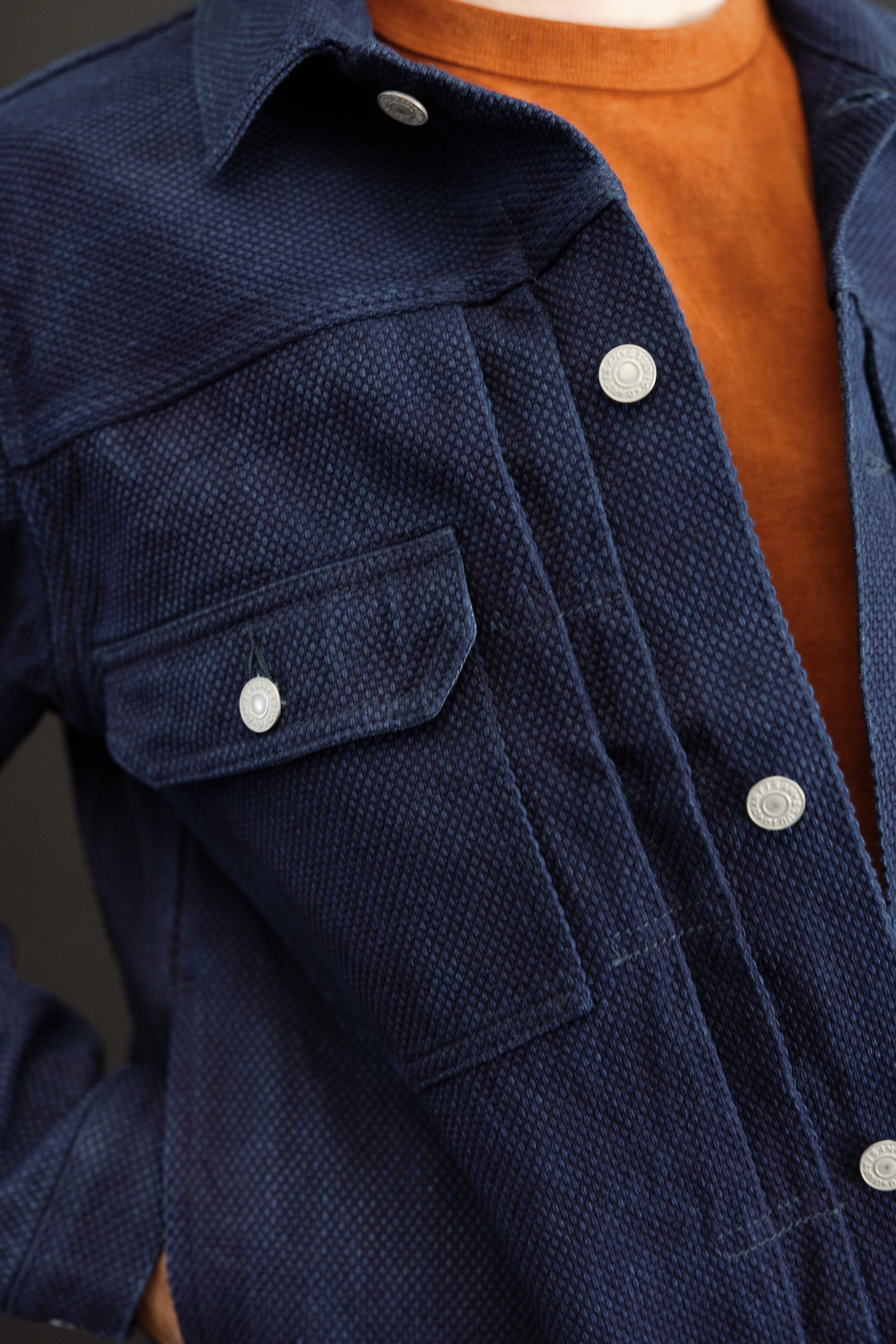 Close-up front view of navy textured shirt with silver buttons, chest pocket, and collar detail on male model