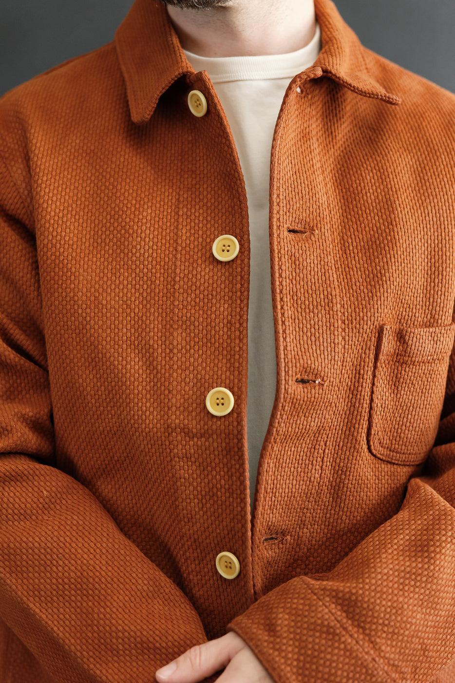 Close-up front view of a male model wearing an orange corduroy shirt featuring button details and texture.