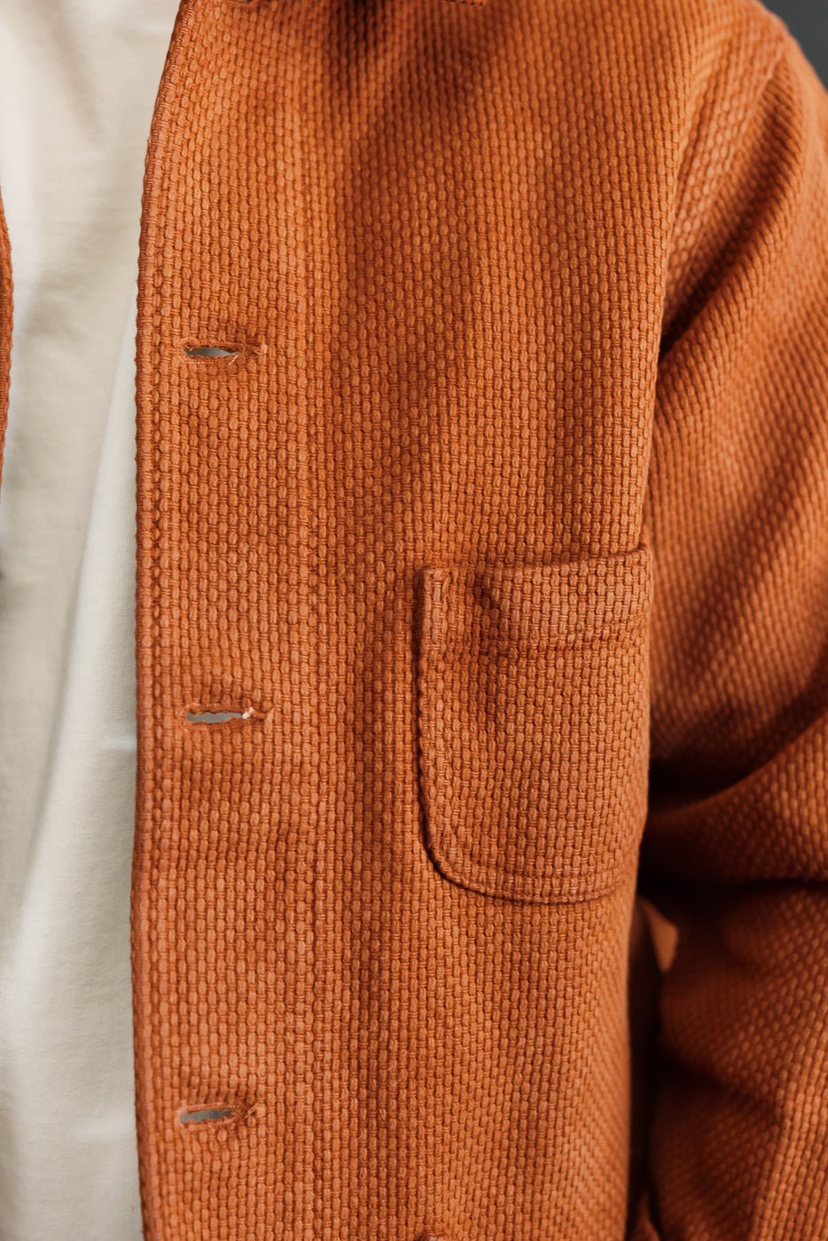 Close-up front view of a burnt orange textured waffle knit chore coat showing pocket and buttons.