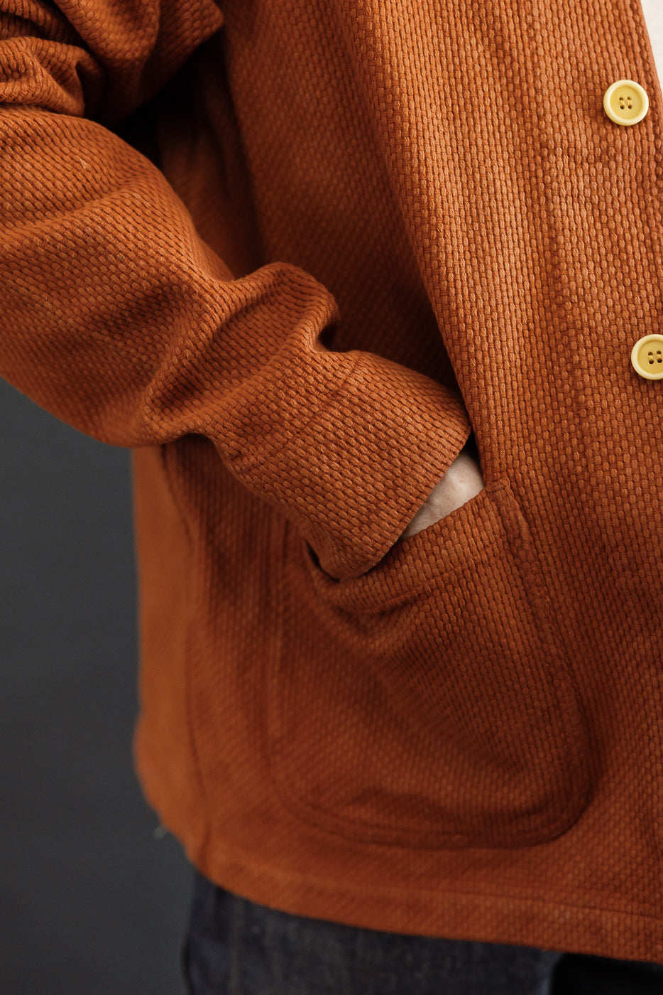 Close-up of the front side of a male model's rust corduroy jacket, showing fabric texture and a pocket.