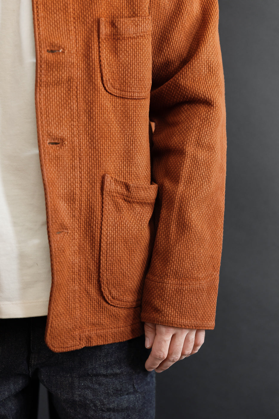 Close-up, front view of a male model wearing a rust-colored corduroy jacket showing pocket and button details.