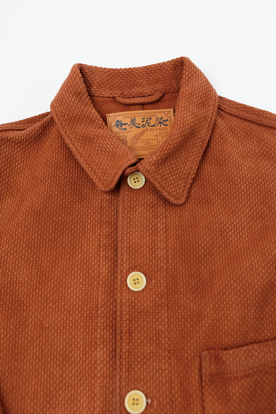 Close-up front view of a rust-colored textured fabric shirt collar and tan buttons.
