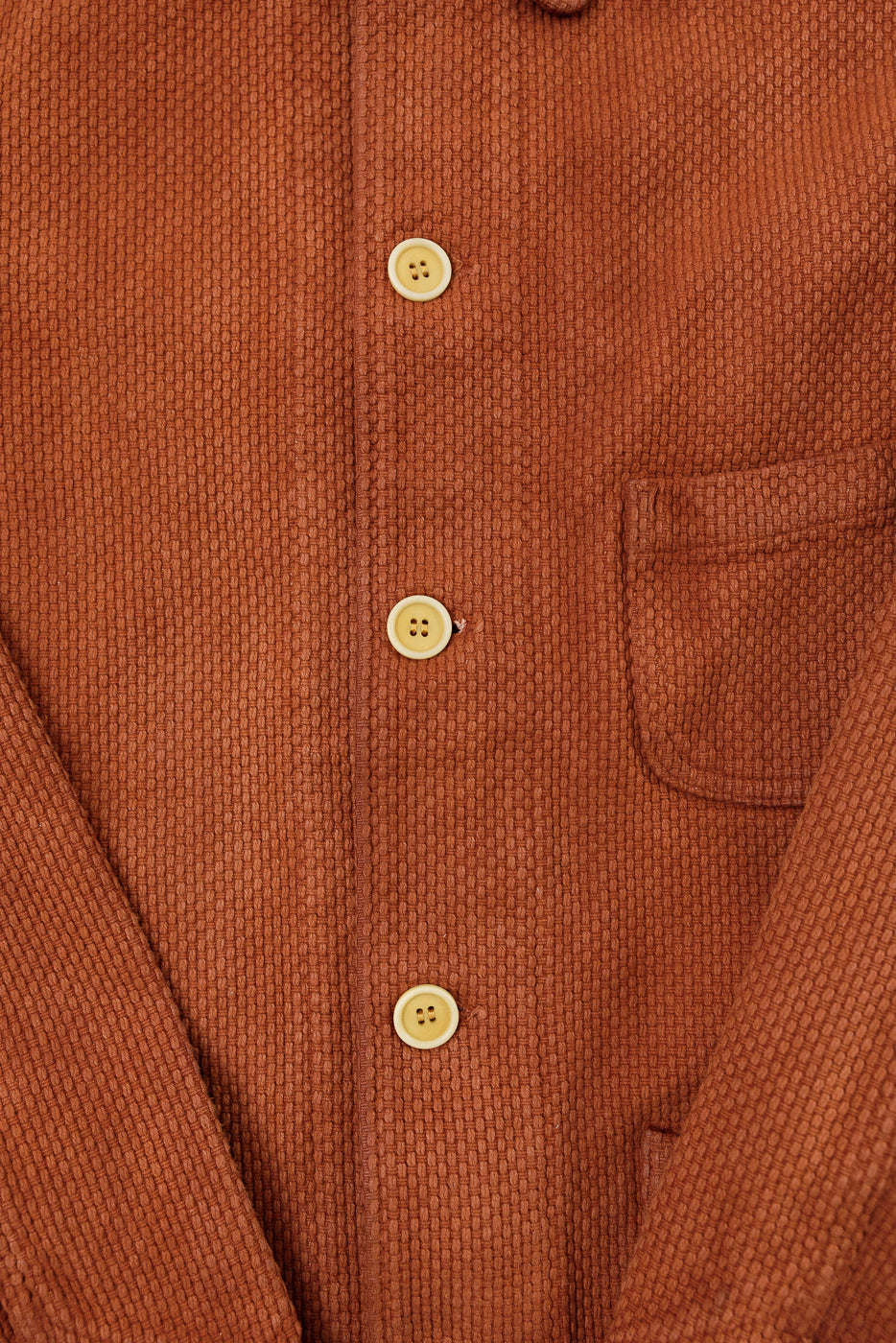 Close-up front view of rust orange textured waffle knit shirt showing buttons and chest pocket.