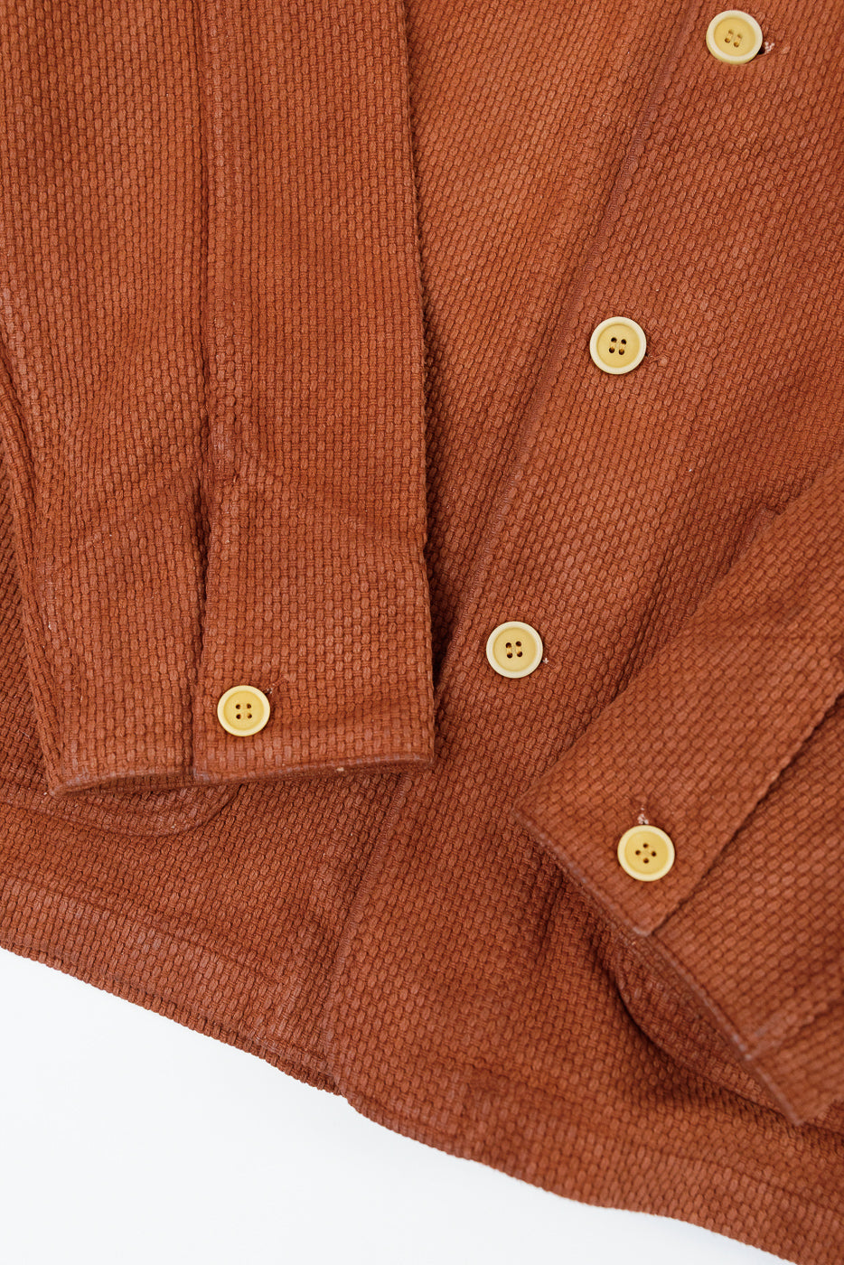 Close-up of the front and sleeves of a brown textured shirt showing buttons and fabric.