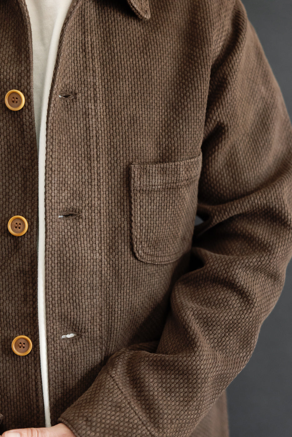 Close-up front view of a brown textured corduroy jacket showing chest pocket and buttons.