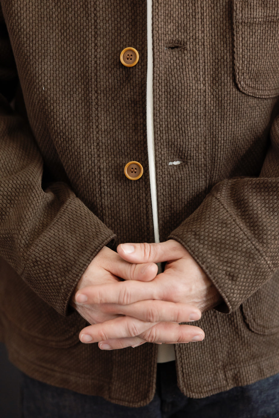 Close-up front view of a male model wearing a brown textured corduroy jacket, focusing on the buttons and fabric detail.