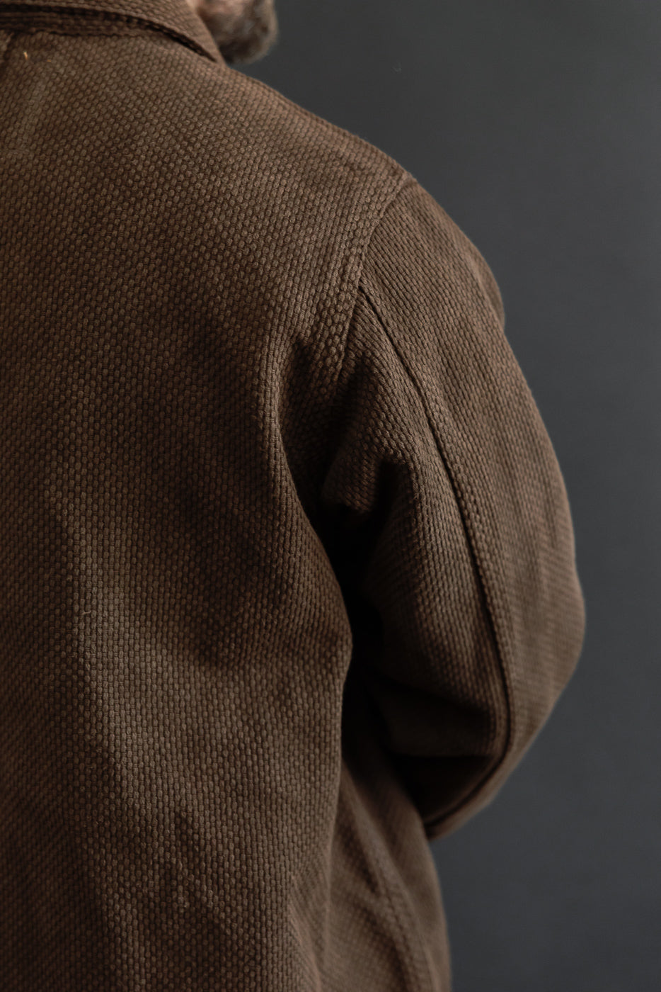 Close-up of the back and shoulder of a brown textured fabric jacket.