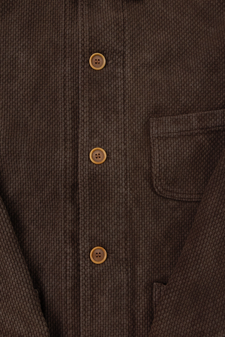 Close-up front view of brown textured fabric shirt showing buttons and chest pocket detail.