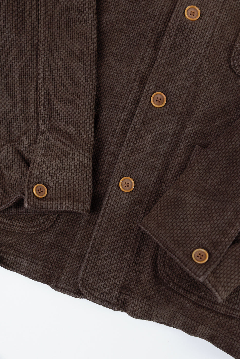Close-up of the front and sleeve of a brown textured fabric jacket showing brown buttons.