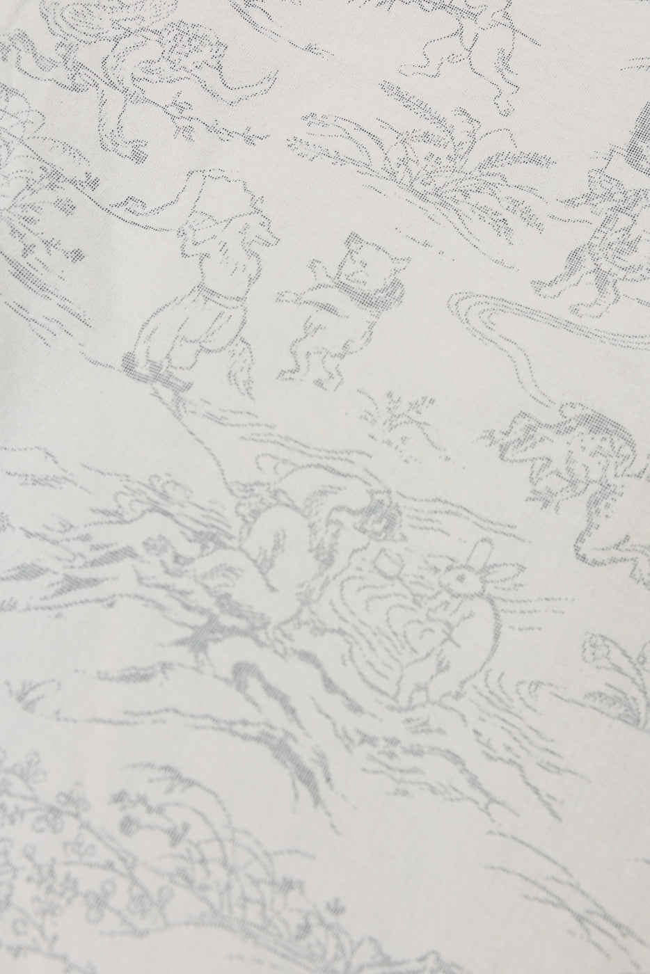 Close-up of white shirt fabric with detailed gray storybook print, showing characters and floral patterns.