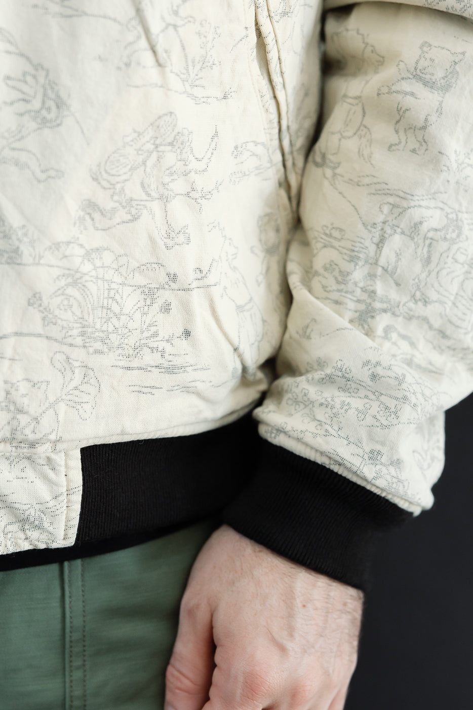 Close-up side view of male model wearing cream patterned jacket with black ribbed cuffs, athletic build