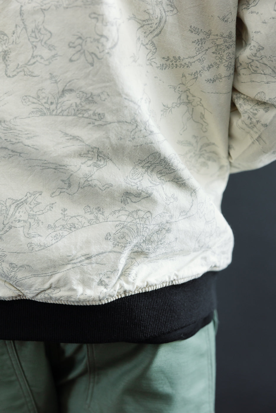 Close-up of male model's side torso showing cream jacket with rabbit print, ribbed hem, and black waistband