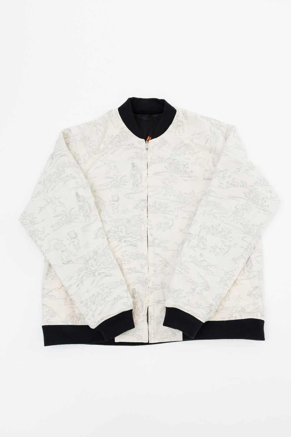 Front flat lay of cream bomber jacket with gray print, black ribbed collar, cuffs, hem; full-zip closure