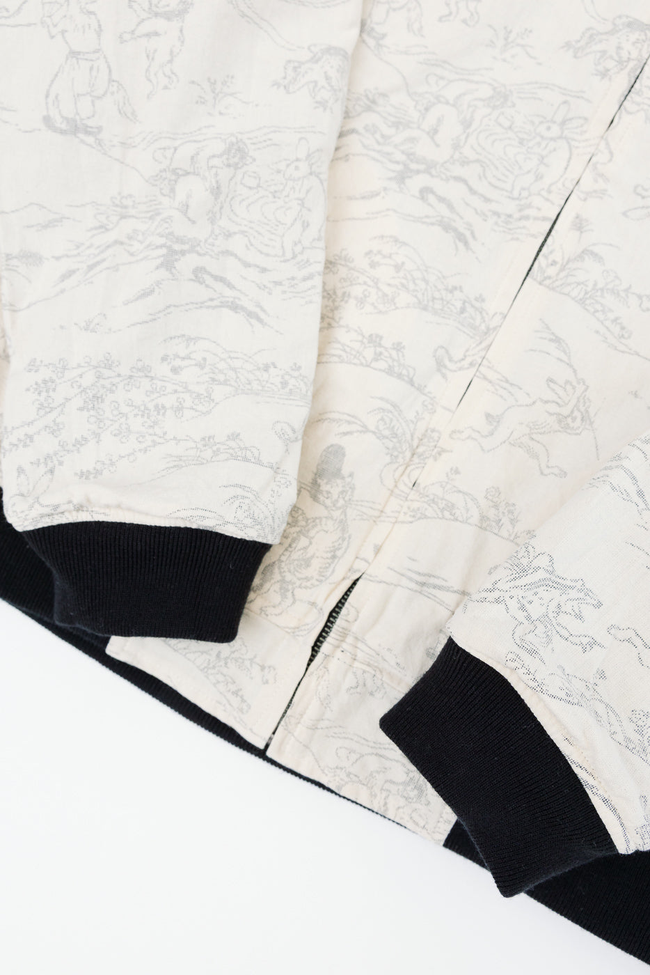 Close-up front view of cream bomber jacket with gray animal print, black ribbed cuffs and hem, zipper detail