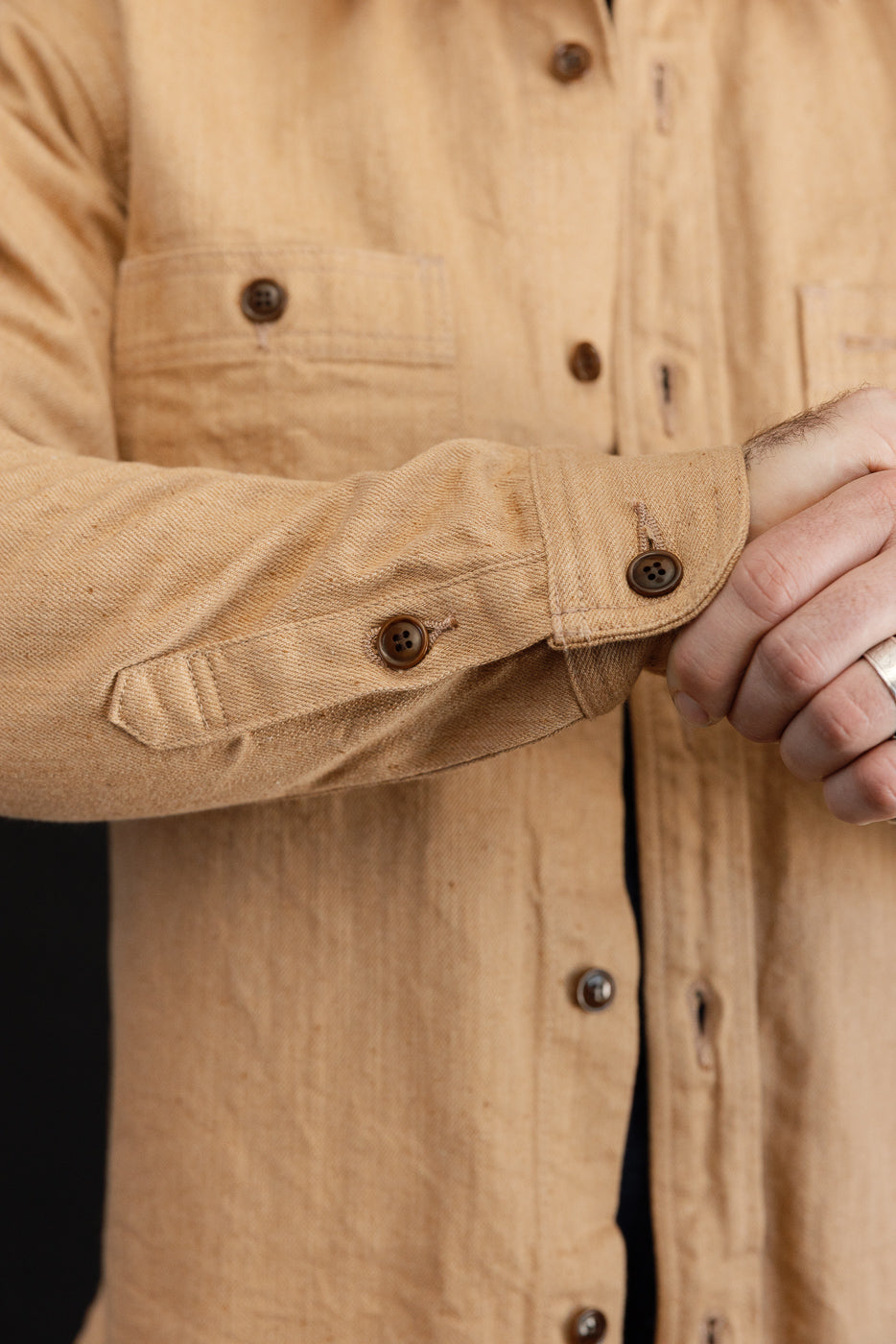 Close-up of male model's arm showing tan shirt sleeve with buttoned cuff and fabric texture
