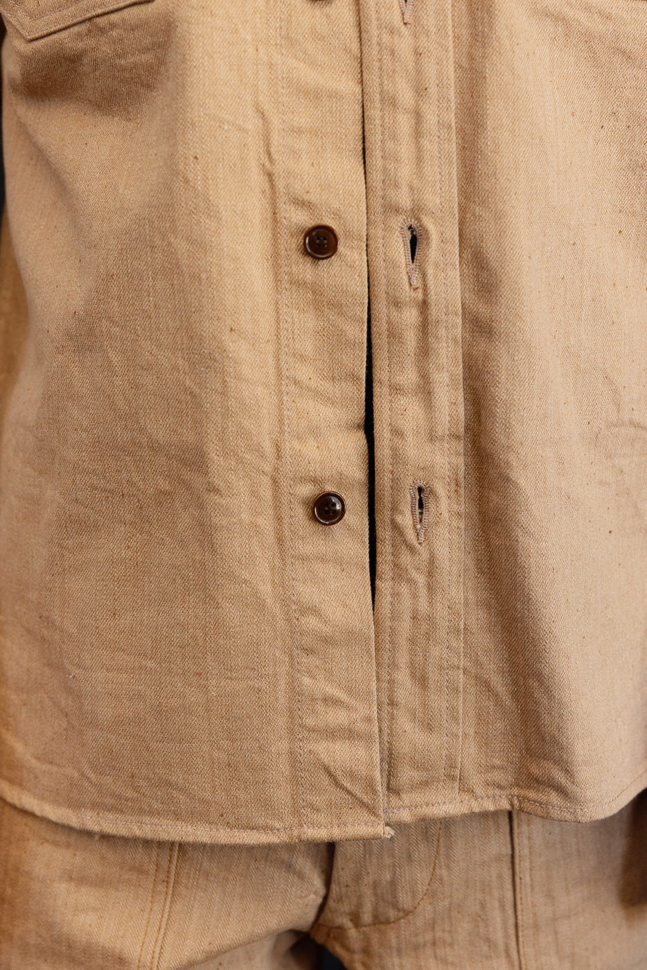 Close-up front view of tan shirt with brown buttons and fabric texture, worn by male model