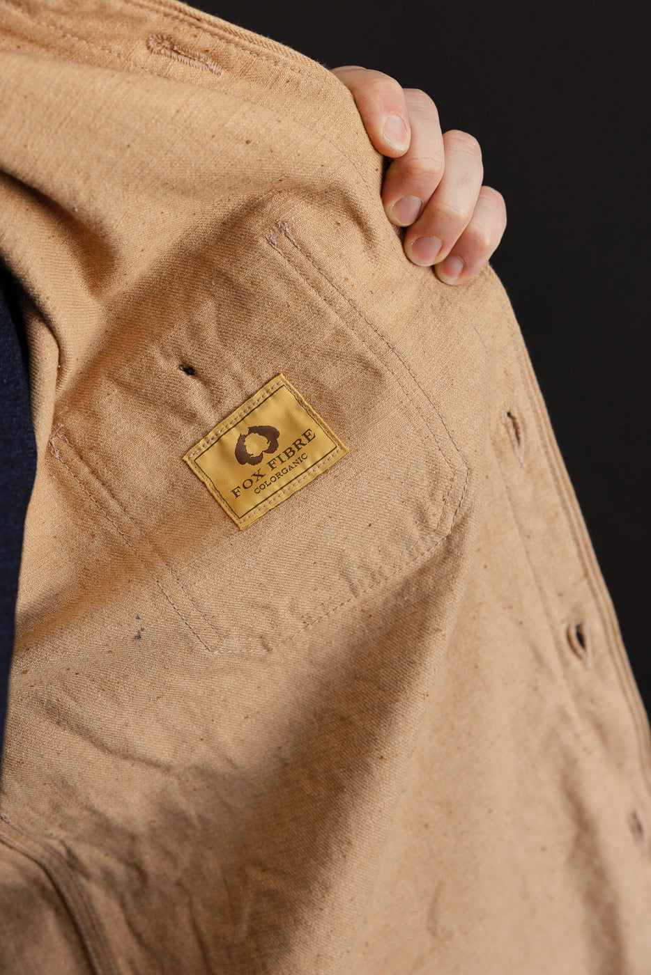 Close-up of tan work shirt front pocket with Fox Fibre tag, showing fabric texture and button detail