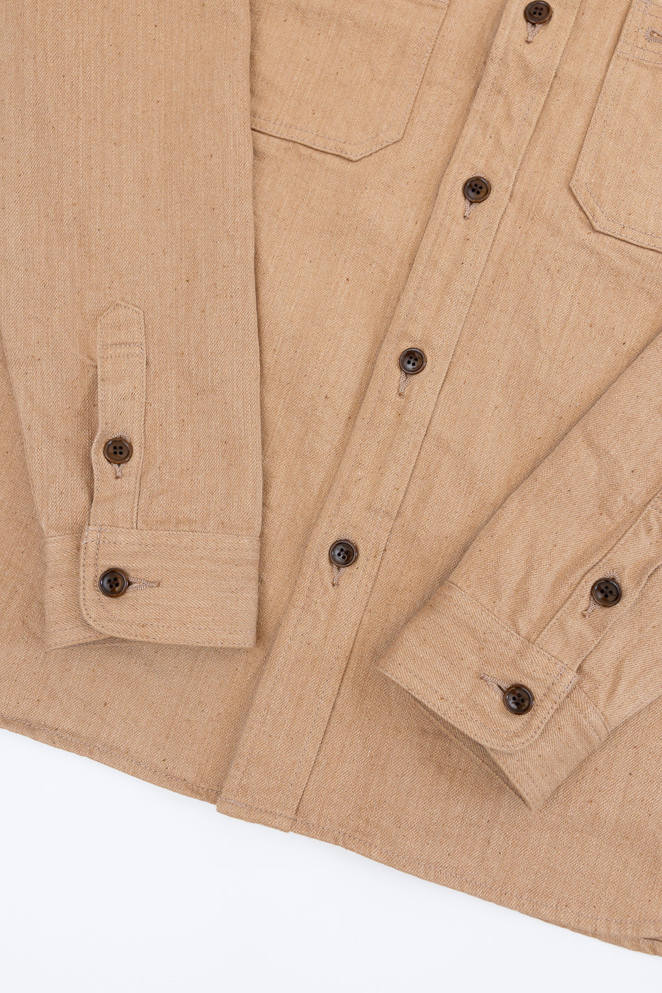 Close-up front view of tan work shirt with button cuffs, chest pockets, and dark buttons on textured fabric
