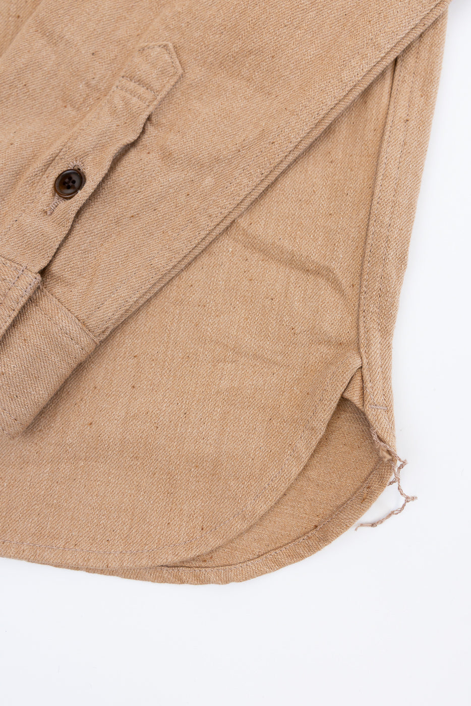 Close-up front view of tan shirt hem with raw edge, button placket, and textured fabric detail