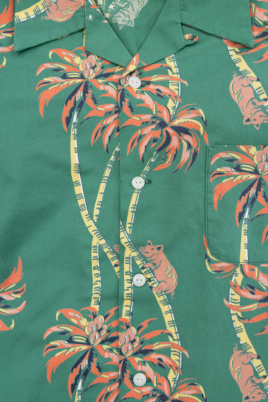 Close-up front view of green tropical print shirt with palm trees, pigs, white buttons, and chest pocket