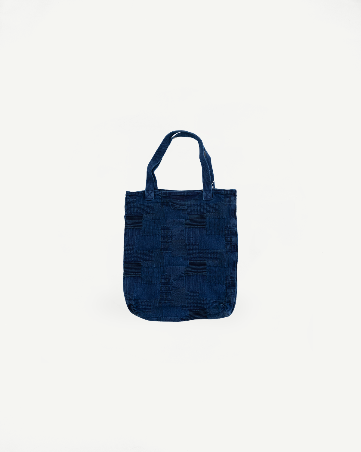 Front view of navy blue patchwork denim tote bag with textured weave pattern and sturdy handles, flat lay