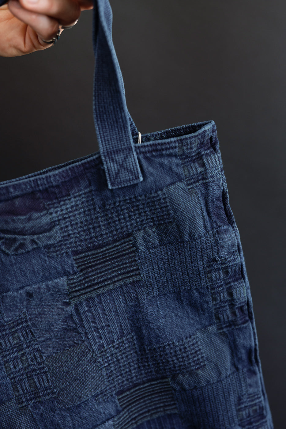 Close-up of indigo patchwork tote bag front, showing textured denim panels, sturdy handle, and top stitching detail