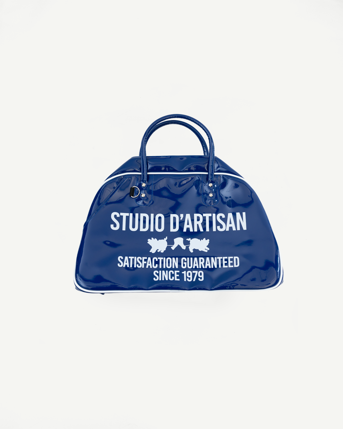 Blue glossy duffel bag front view, 'STUDIO D'ARTISAN' text, white trim, handles, satisfaction guarantee since 1979