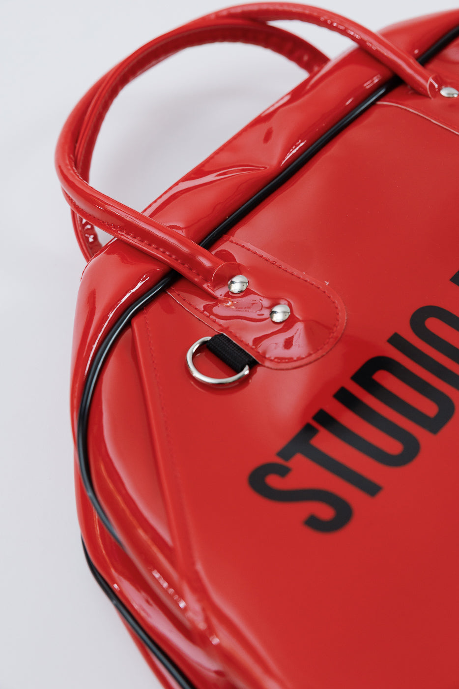 Close-up of red glossy bag front, showing black text, handles, and silver hardware details.