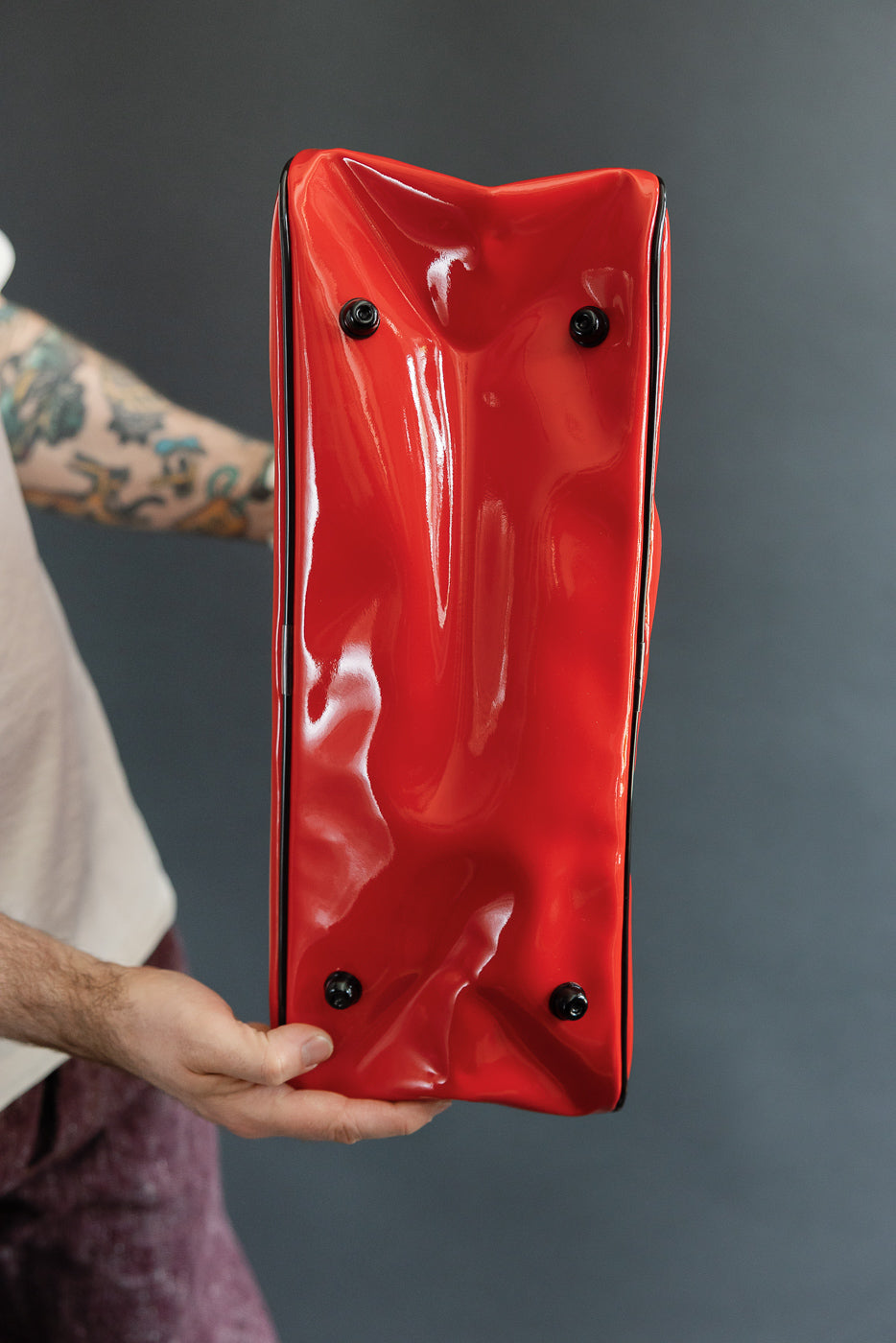 Close-up of red glossy bag bottom with black feet, held by male model