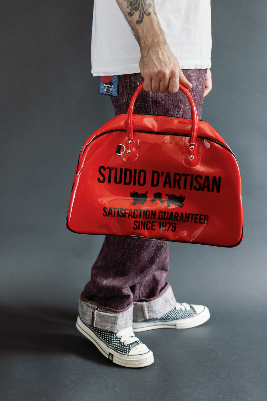 Male model holding red Studio D'Artisan bag, front view, full body, athletic build, casual attire