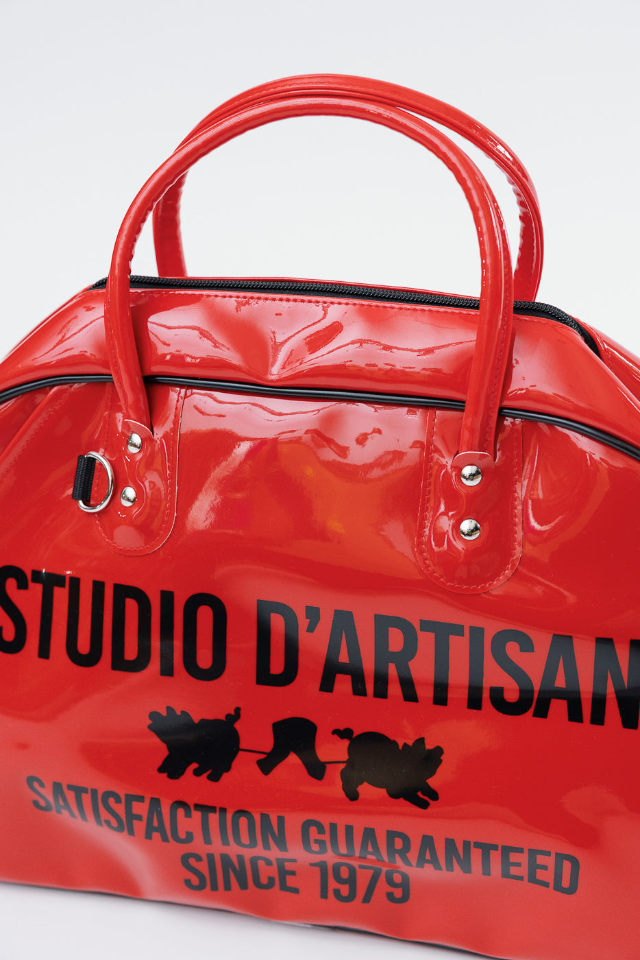 Red glossy duffel bag with 'Studio D'Artisan' print and pig graphic, front view