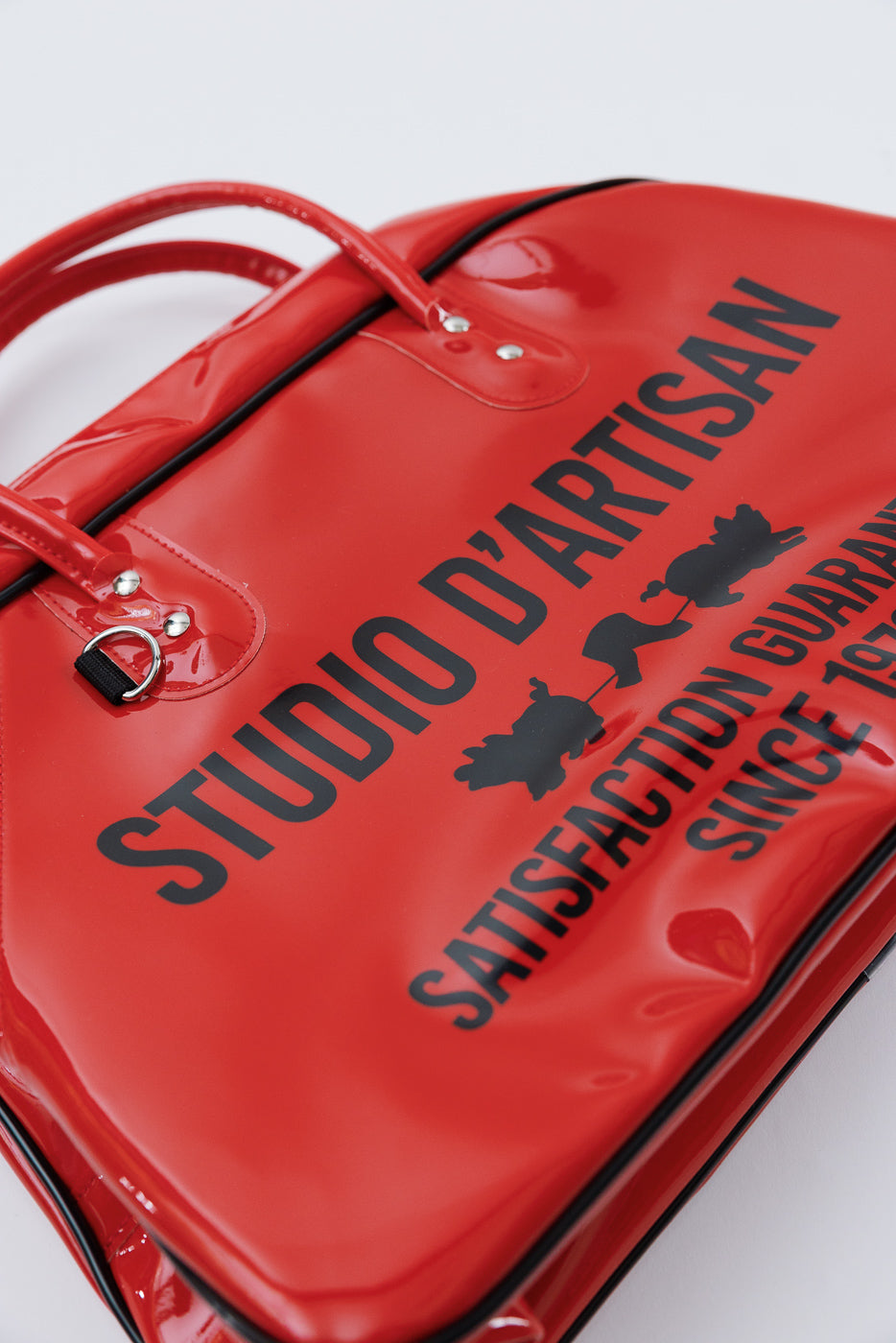 Close-up of red glossy bag front, showing 'STUDIO D'ARTISAN' text and pig graphics with black trim.
