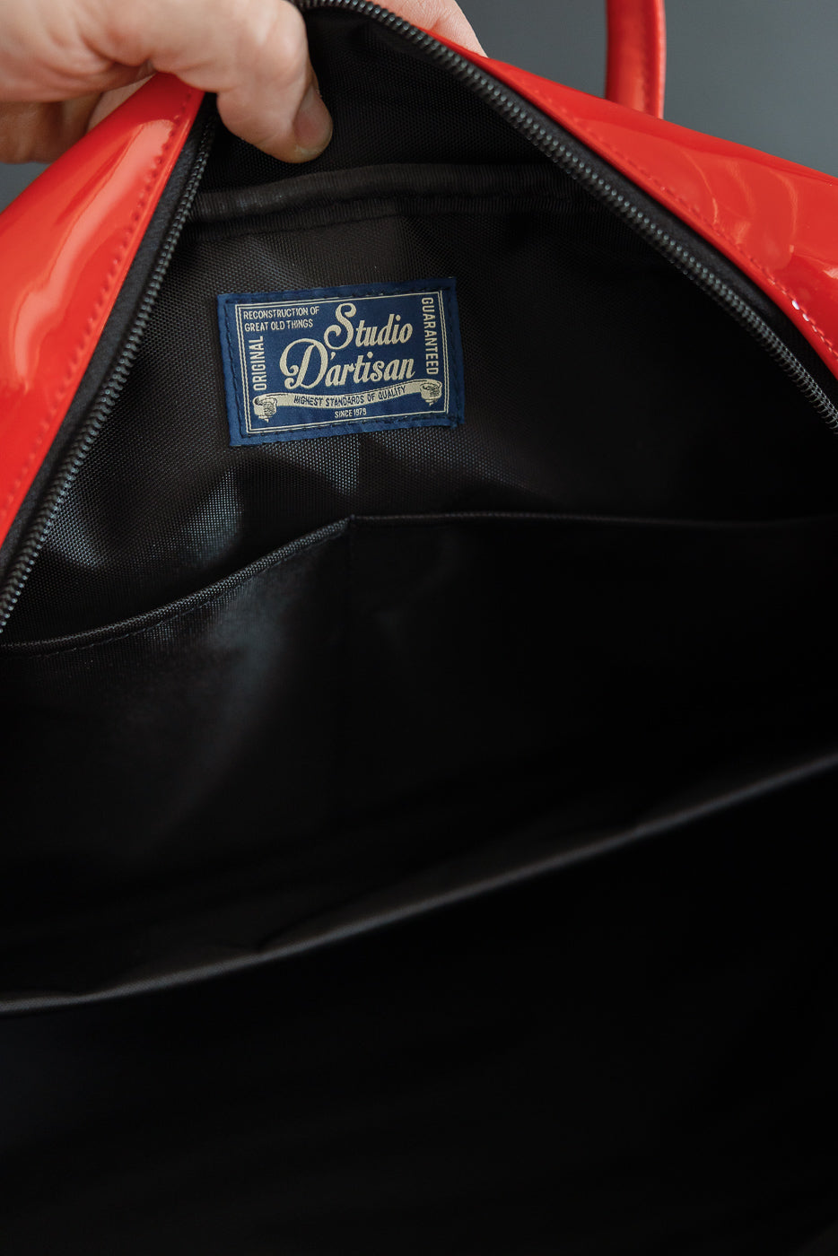 Close-up of red bag's interior showing Studio Dartisan label, black lining, and zipper detail.
