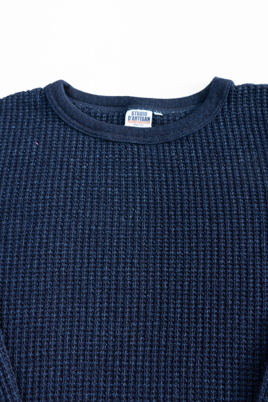 Close-up of front chest and collar of indigo-dyed heavy waffle thermal shirt, showing texture and neck tag.