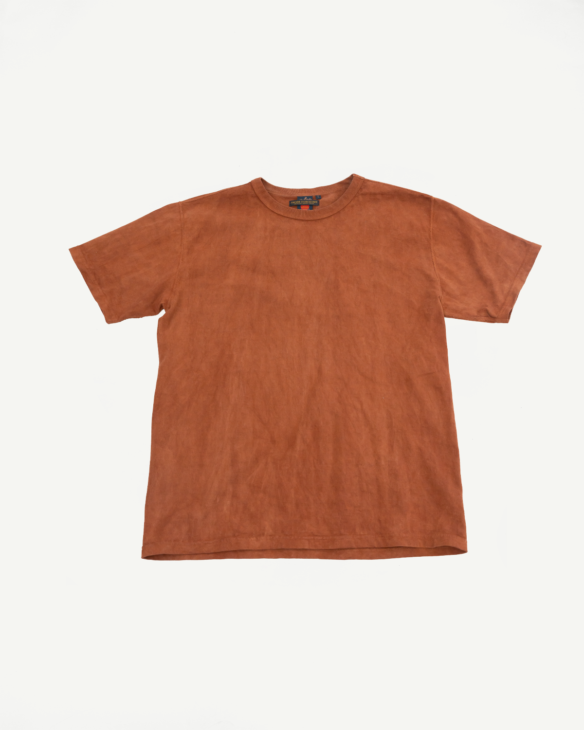 Front flat lay of rust-colored short-sleeve tee with tag detail, showcasing fabric texture and hem style