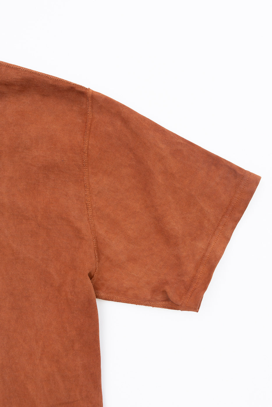 Close-up front view of rust-colored t-shirt showing sleeve hem and shoulder seam detail, soft textured fabric
