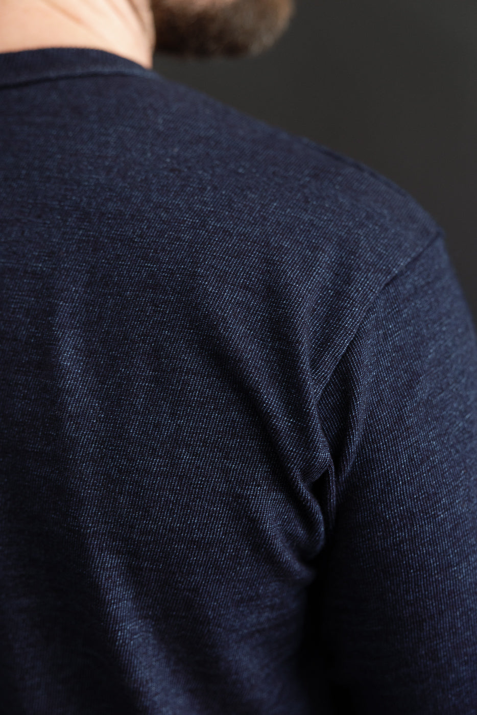 Close-up back view of male model in dark blue textured shirt, showcasing shoulder seam and fabric detail.