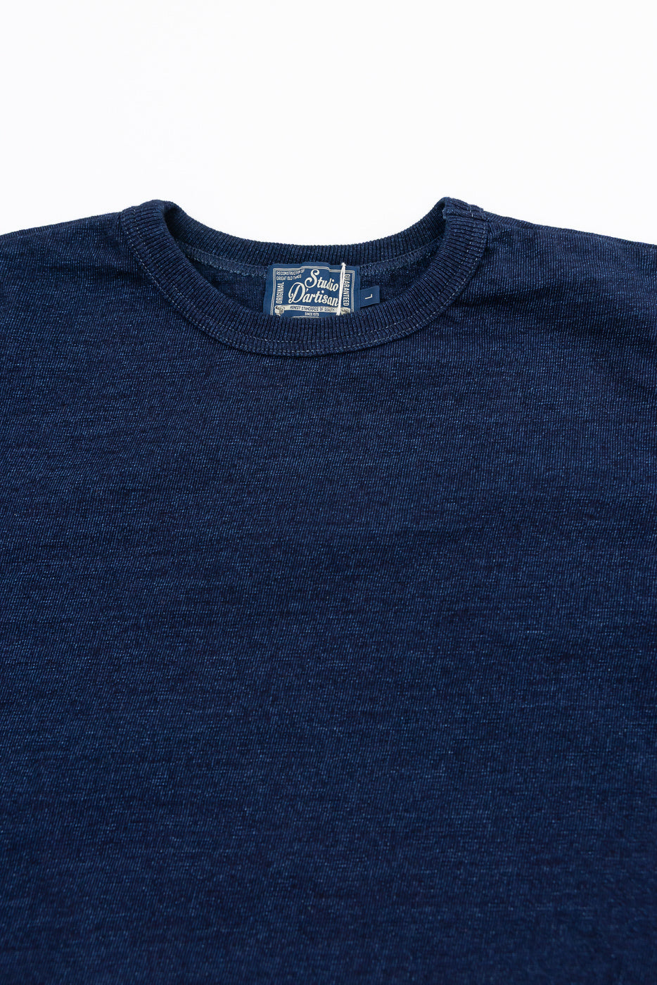Close-up front view of navy blue crewneck tee showing ribbed collar and Studio D'Artisan tag detail