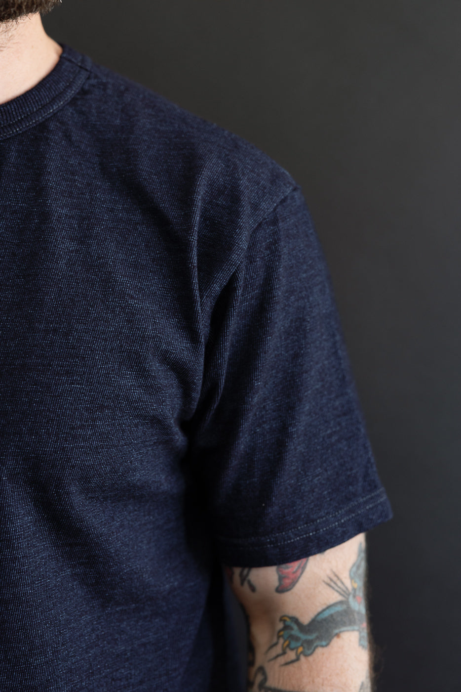 Close-up of male model's shoulder and sleeve, showcasing dark denim texture and hem detail.