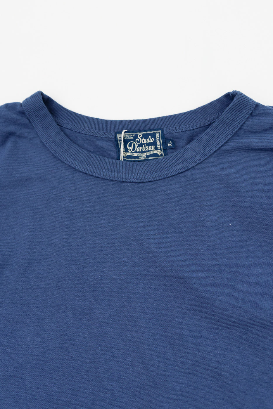 Close-up front view of navy blue t-shirt showing Studio D'artisan tag, ribbed crew neck, size XL