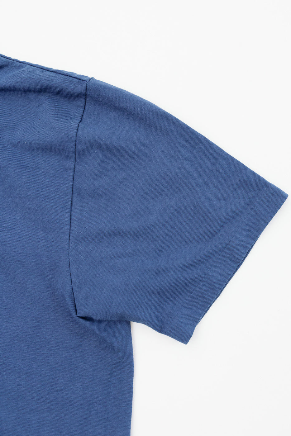 Close-up front view of blue t-shirt sleeve and shoulder seam, showing fabric texture and construction details