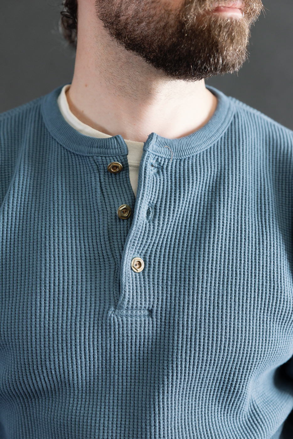 Close-up front of Studio D'Artisan blue heavy thermal henley, male model 5'9 165lbs athletic build, showing textured waffle knit, three buttons, and ribbed collar.