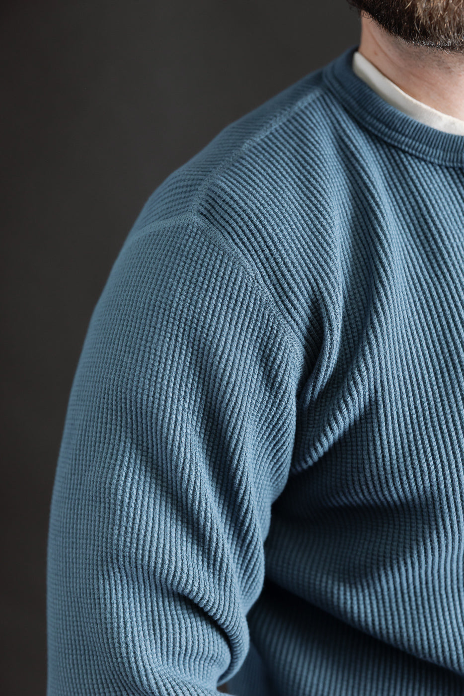 Close-up of male model shoulder in blue heavy thermal long sleeve henley, front left view, textured ribbed cotton